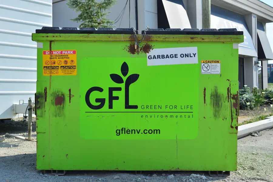 A lime green GFL Environmental front-load bin with a black lid, in a parking lot