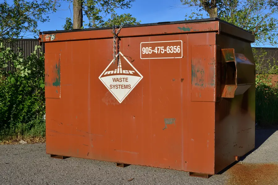 A rust orange Miller Waste Systems front-load bin with its diamond badge